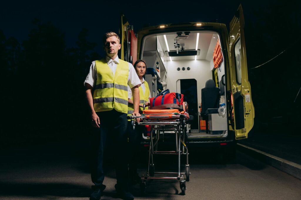 a man and a woman standing beside the stretcher and an ambulance
