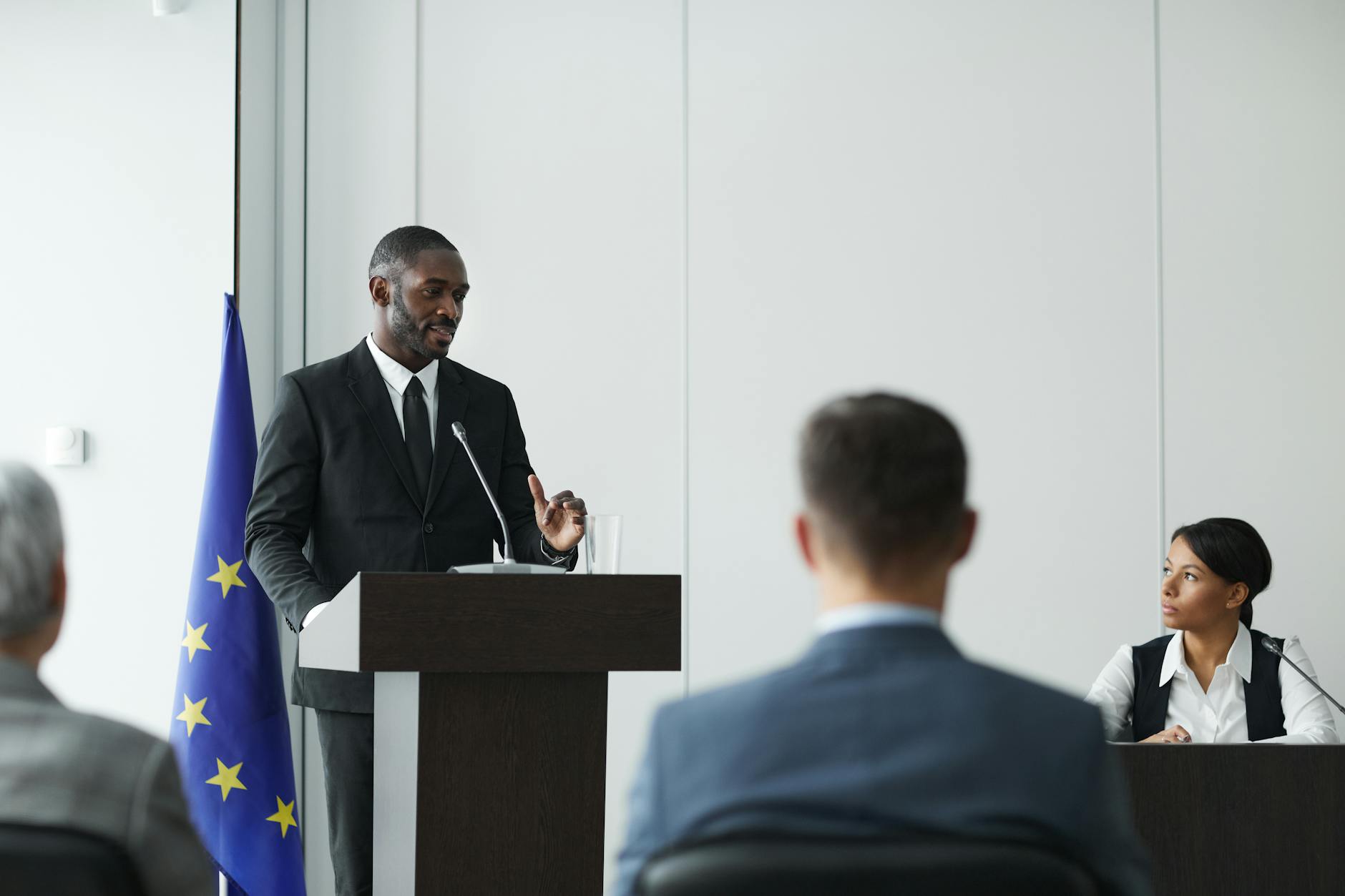 a man in black suit speaking in front of people